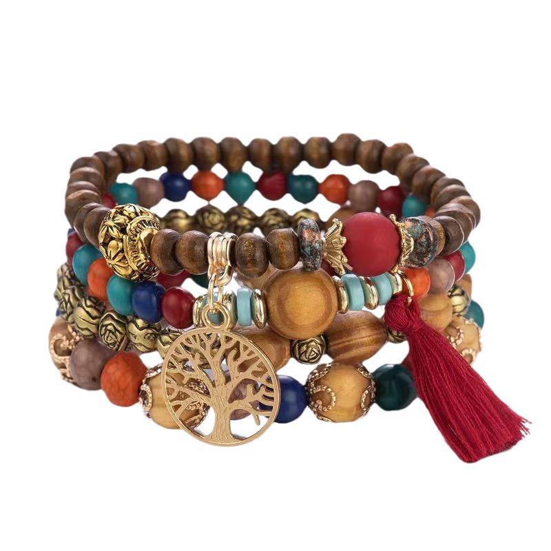 Bracelet à plusieurs rangs de perles brunes, rouges, orange, bleues et turquoise, avec un pendentif doré arbre de vie et un pompon rouge, sur fond blanc.
