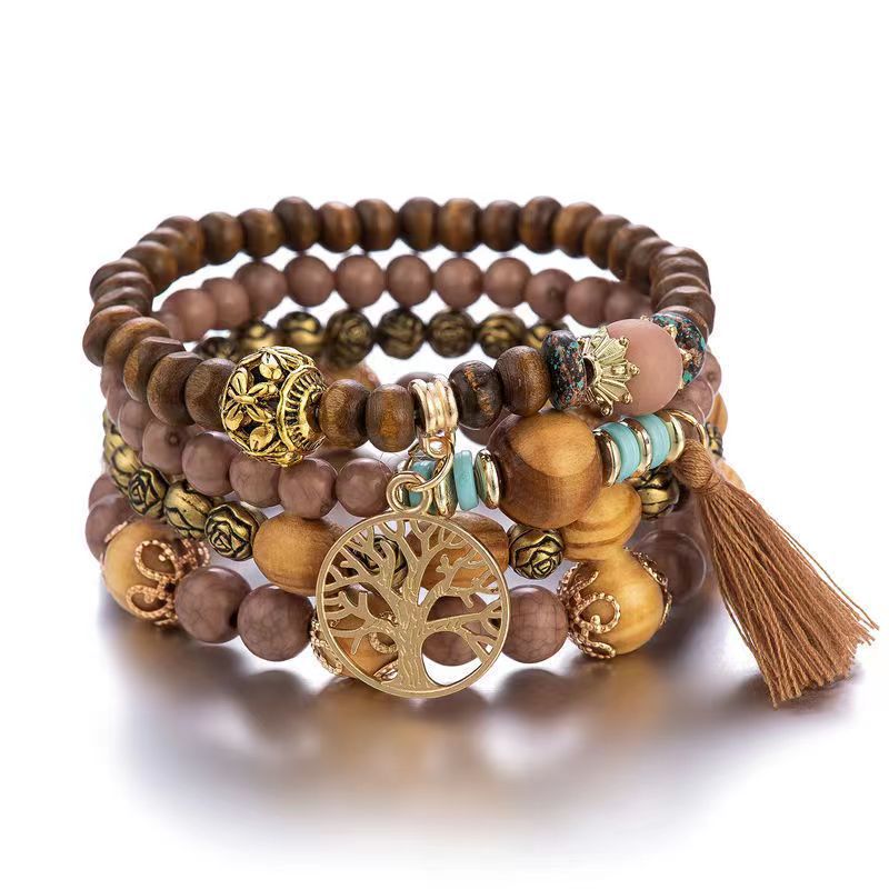 Bracelet à plusieurs rangs de perles brunes et beige rosé, avec des touches turquoise, un pendentif doré arbre de vie et un pompon brun, sur fond blanc.