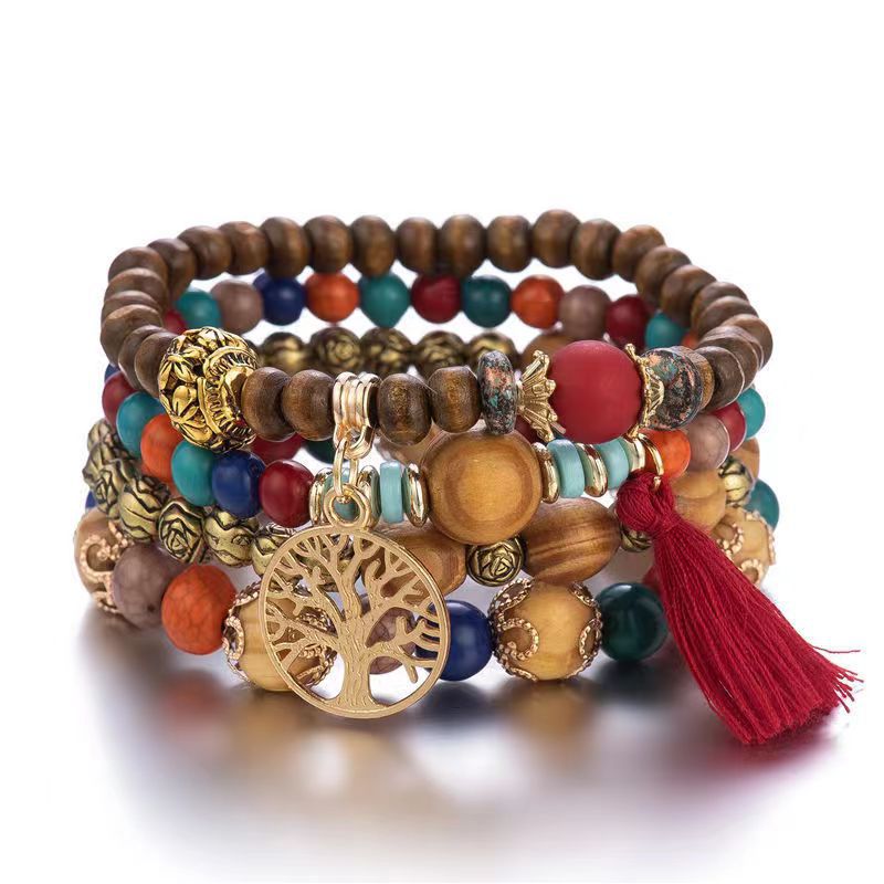 Bracelet à plusieurs rangs de perles brunes et multicolores, avec un pendentif doré arbre de vie et un pompon rouge, sur fond blanc.