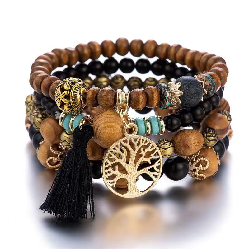 Bracelet à plusieurs rangs de perles noires, brunes et turquoise, avec un pendentif doré arbre de vie et un pompon noir, sur fond blanc.