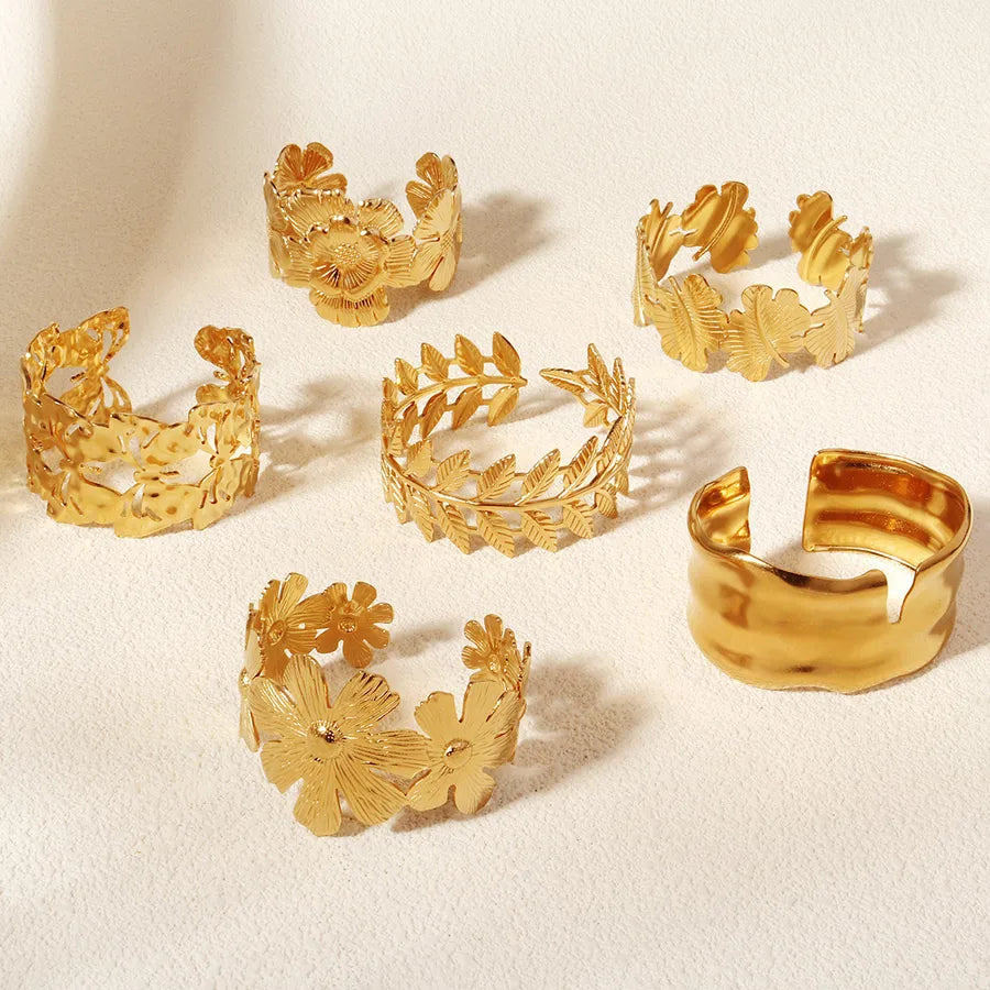 Six bracelets dorés, dont cinq à motifs floraux ou de feuilles et un jonc lisse, sur fond beige