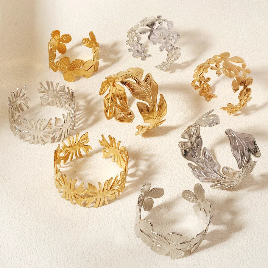 Huit bracelets joncs à motifs floraux dorés et argentés disposés sur un fond beige