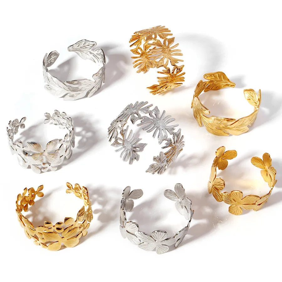 Huit bracelets ouverts dorés et argentés à motifs de fleurs et de feuilles, disposés sur fond blanc